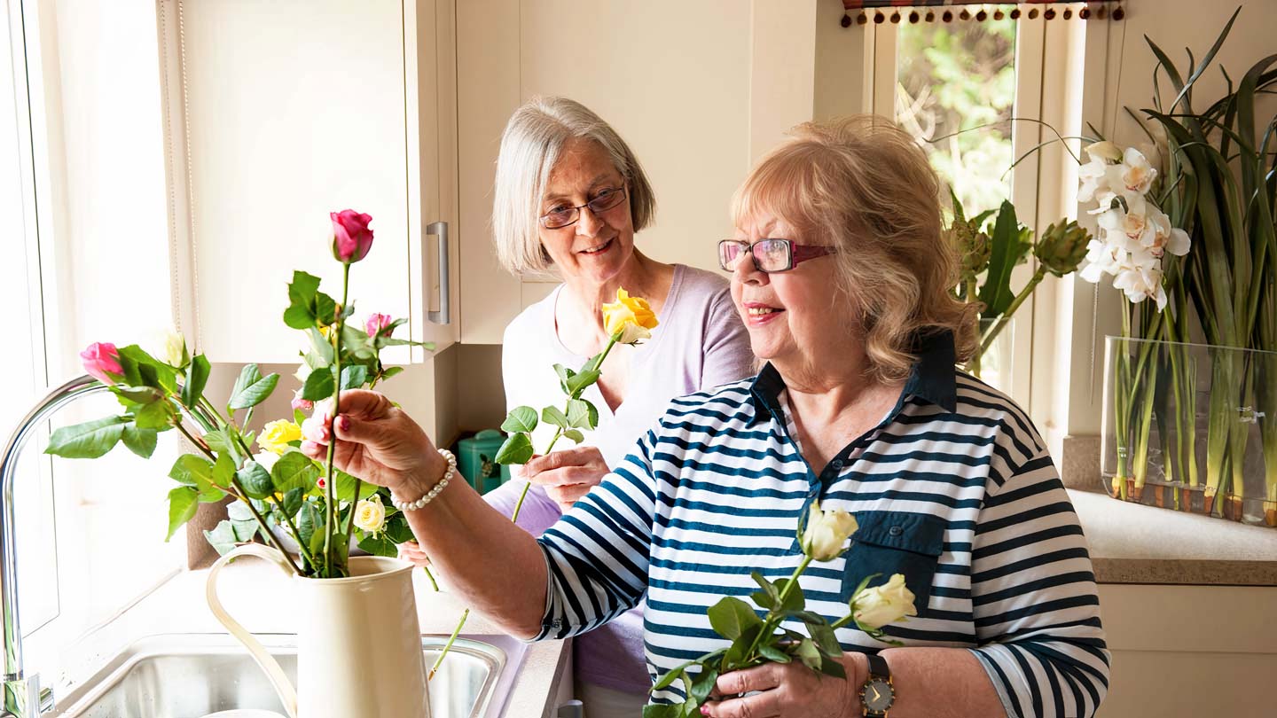 Two women gracefully arranging flowers in a vase, creating a beautiful centrepiece with vibrant colours.